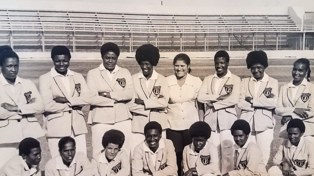 Historic 1976 West Indies women’s cricket team group photo featuring players and staff posing at a cricket stadium in black and white.