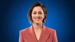 Former Australian women's cricket team vice-captain Rachael Haynes smiling in a pink blazer against a blue background. Copy Alt Text