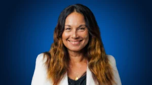 New Zealand Cricket (NZC) Board Chair Diana Puketapu-Lyndon smiling in a white blazer during an official portrait against a blue background.