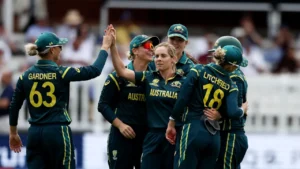 Australia women's cricket team players celebrate a wicket during an international cricket match, with teammates high-fiving on the field.