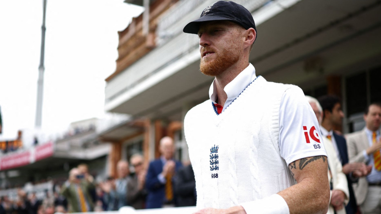 Ben Stokes walking onto the field in England Test cricket whites at Lord's Cricket Ground during a match, with spectators in the background.