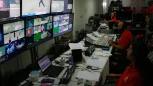 Broadcast production team operating video switching and monitoring equipment in a live control room with multiple screens displaying event coverage.
