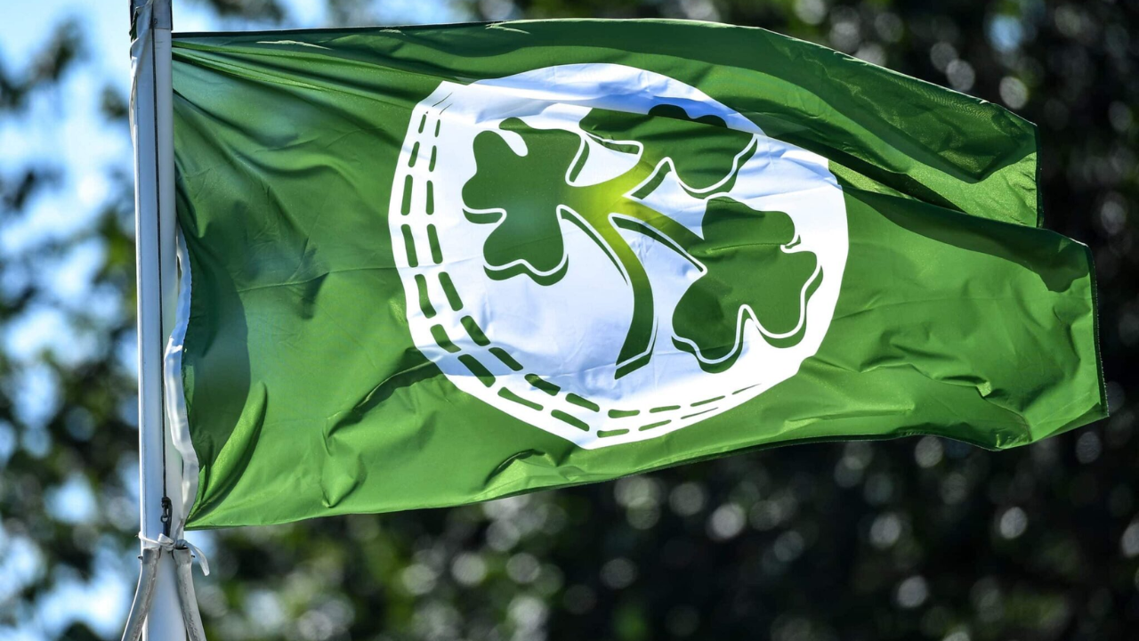 Cricket Ireland flag featuring the shamrock logo waving outdoors against a blurred background, representing Irish cricket.