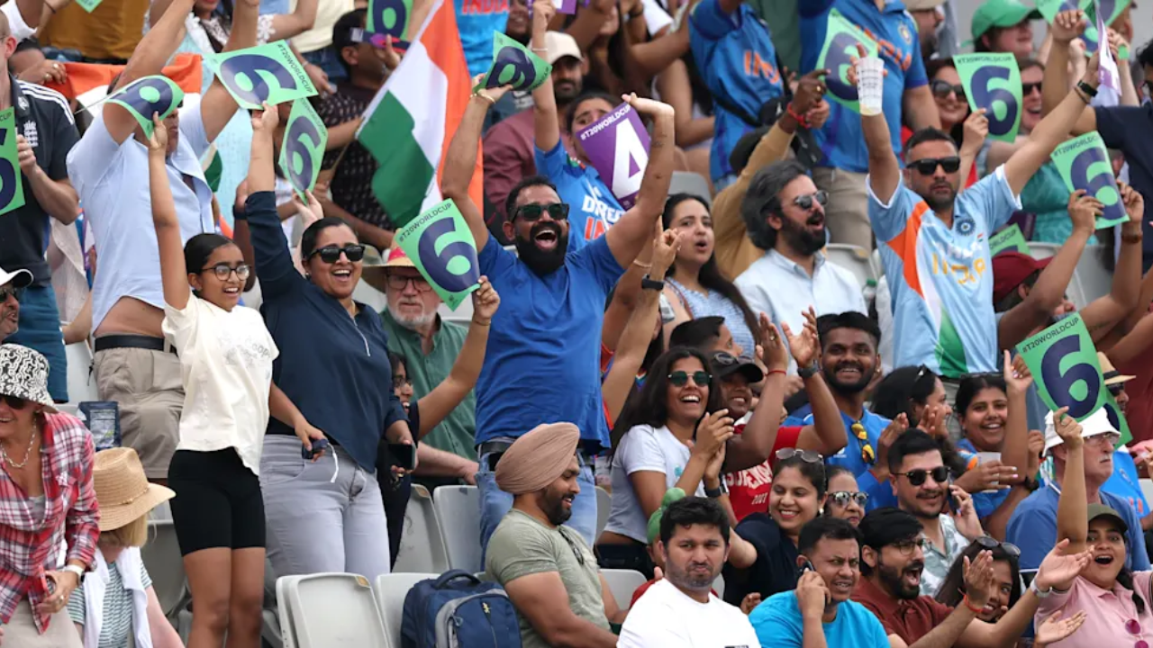 India cricket fans cheer in the stadium while holding six-run placards and waving the Indian flag during an international cricket match.