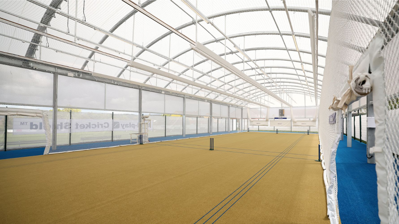 Indoor cricket training facility with practice nets, synthetic pitch surface, and covered batting lanes designed for year-round cricket coaching and player development.