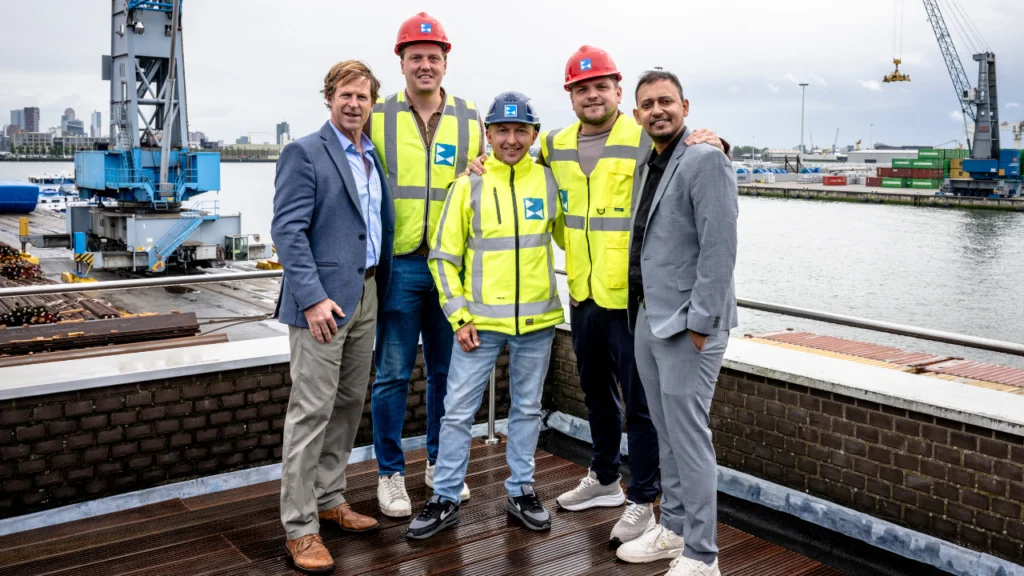 Jonty Rhodes and Shree pose with Rotterdam dockworkers at a port facility in Rotterdam, Netherlands, during a visit highlighting community engagement and local industry connections.