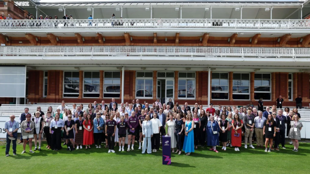 Participants, players, and officials gathered at Lord's Cricket Ground for a women's cricket event linked to The Hundred, posing for a group photograph on the outfield.