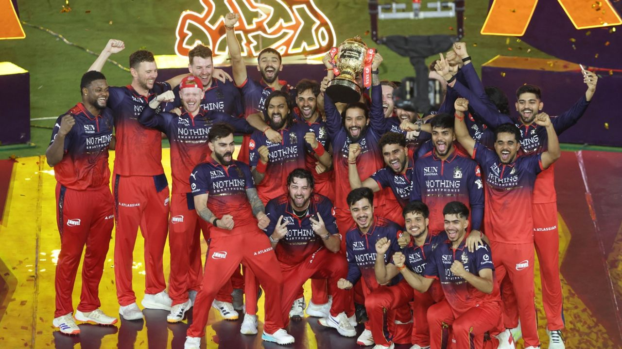 Royal Challengers Bengaluru players celebrate with the IPL trophy after winning the Indian Premier League title, posing together during the championship presentation ceremony.