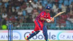Rishabh Pant batting for Lucknow Super Giants during an IPL match, playing a shot while wearing the team's red and blue jersey in front of a packed stadium crowd.
