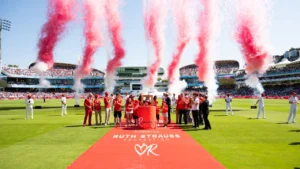 Ruth Strauss Foundation charity ceremony at a packed cricket stadium with participants gathered on the pitch as red and white smoke effects are launched during a fundraising event.