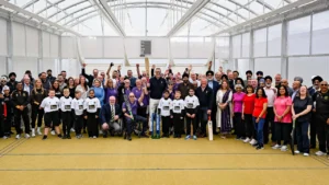 Participants, community members, and young cricketers gather for a group photo inside the Cricket Dome at Sporting Khalsa FC following a cricket development and community engagement event.