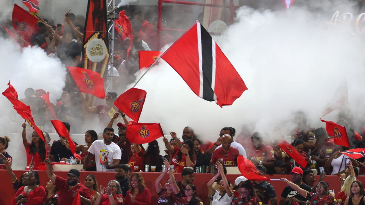 Trinbago Knight Riders supporters waving team flags and the Trinidad and Tobago national flag amid celebrations during a Caribbean Premier League (CPL) cricket match.