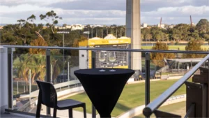 View of WACA Ground in Perth from a hospitality balcony with a table and two wine glasses overlooking the cricket stadium.