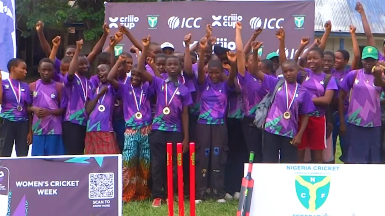 Participants celebrate during ICC Women's Cricket Week in Nigeria, wearing medals and posing in front of Nigeria Cricket Federation and ICC branding at a community cricket development event.