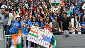 Indian cricket fans cheer with flags and a 'Jambhumi vs Karambhumi' banner during the India vs New Zealand cricket match at a packed stadium.