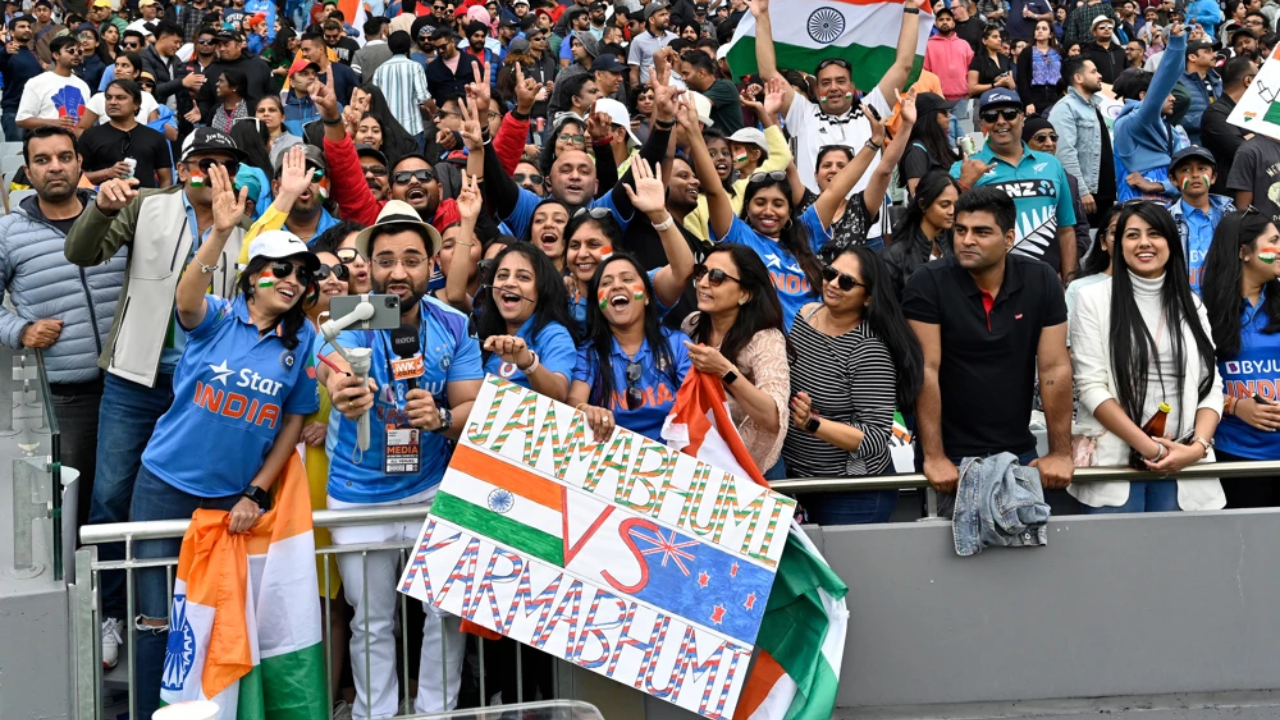 Indian cricket fans cheer with flags and a 'Jambhumi vs Karambhumi' banner during the India vs New Zealand cricket match at a packed stadium.