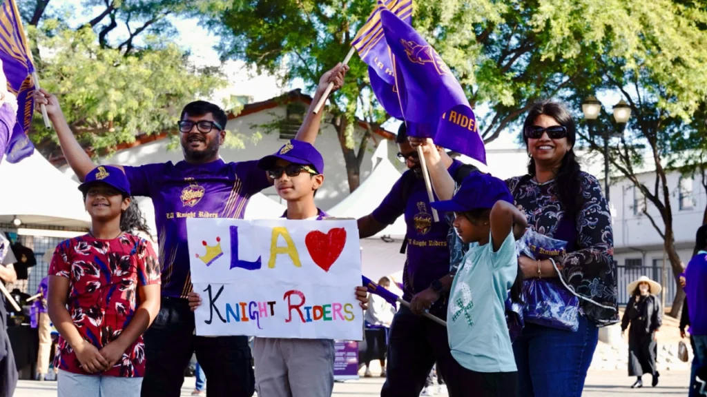 LA Knight Riders fans waving team flags and holding a support banner at Knight Riders Cricket Ground in Los Angeles during a Major League Cricket match.