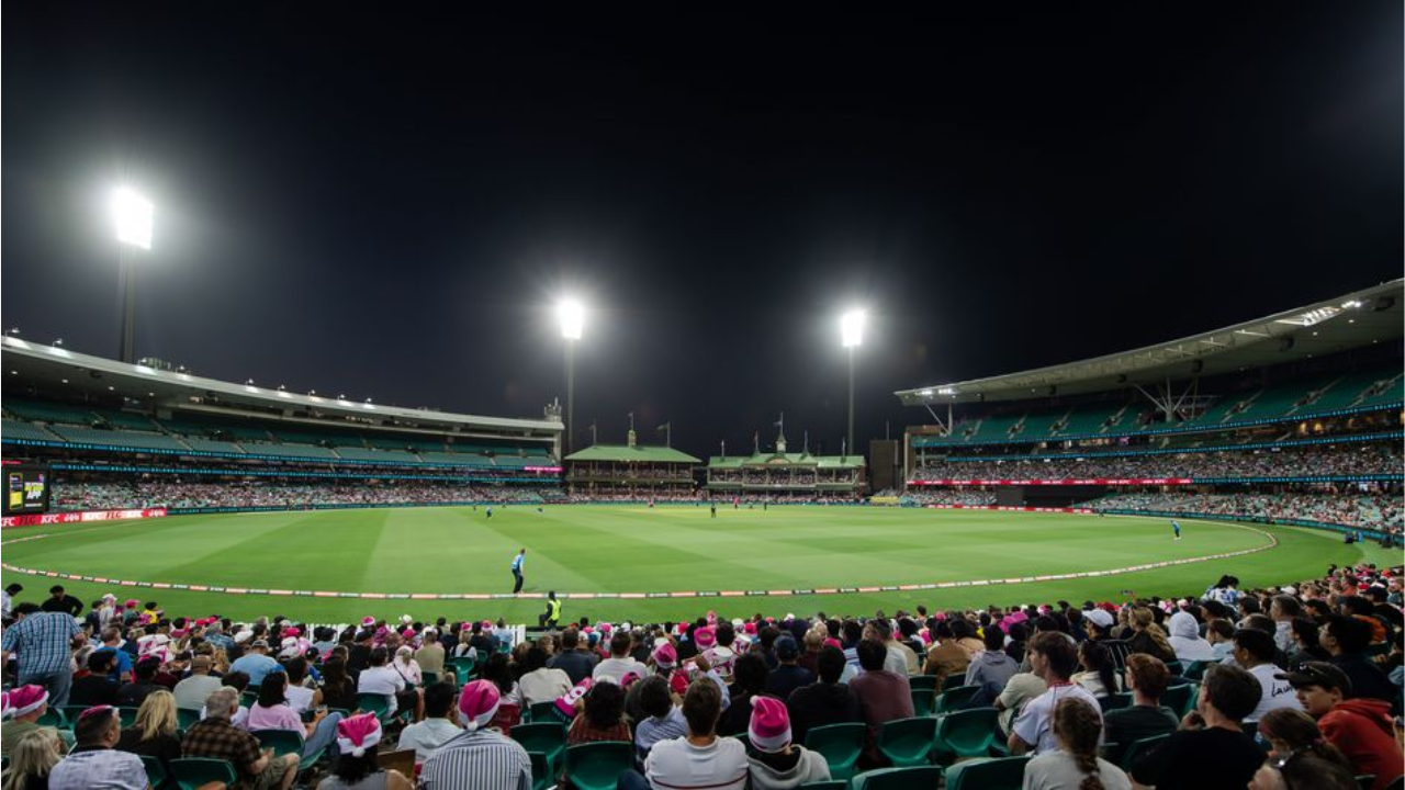 Wide-angle view of the Melbourne Cricket Ground (MCG) during a Big Bash League (BBL) night match, with players on the field under floodlights and a large crowd of spectators in attendance.