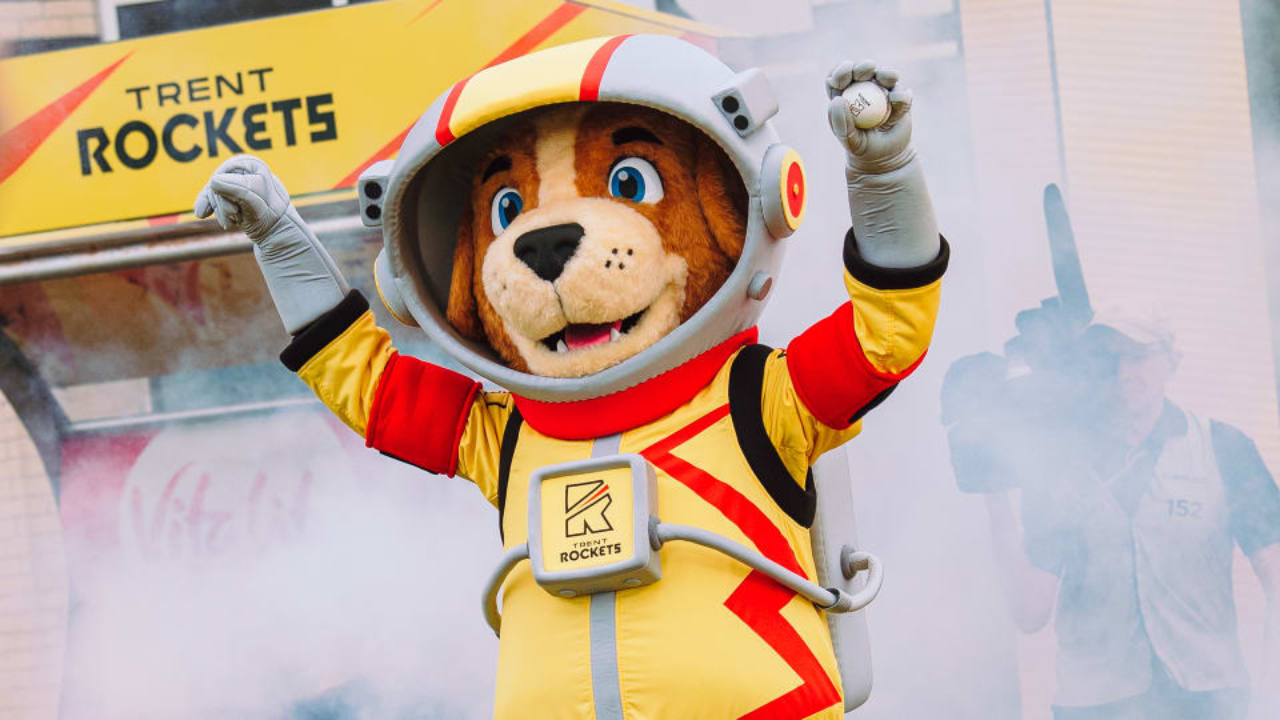 The Trent Rockets mascot entertains fans during a matchday at The Hundred, wearing a space-themed costume in front of Trent Rockets branding.