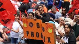 Birmingham Phoenix fans wave team flags and hold banners while supporting their team during a The Hundred cricket match.
