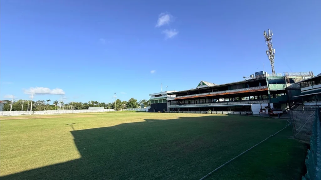 Wide view of the historic Bourda Cricket Ground in Georgetown, Guyana, showing the playing field and iconic pavilion under a clear blue sky.