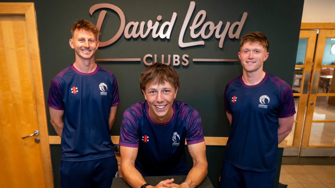 Three Cricket Scotland players pose in front of a David Lloyd Clubs sign as Cricket Scotland announces a new partnership with David Lloyd Leisure.