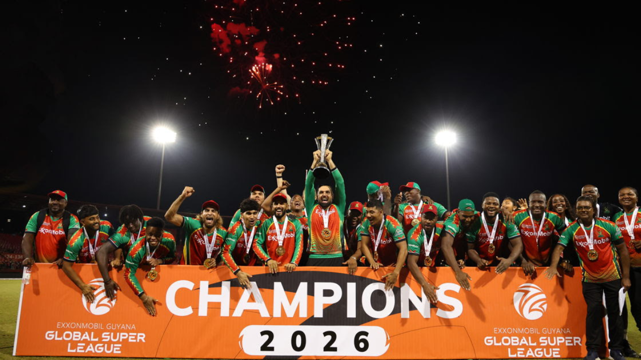 Guyana Amazon Warriors celebrate winning the 2026 Global Super League championship, lifting the trophy as fireworks light up the night sky with teammates wearing medals on the presentation stage.