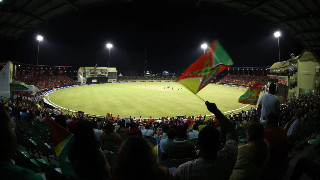 Panoramic night view of Providence Stadium in Guyana during the 2026 Guyana Global Super League, with spectators waving Guyana flags as a match is played.
