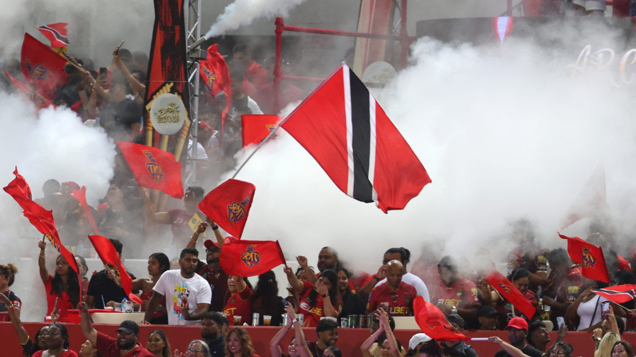 Trinidad Knight Riders fans wave Trinidad and Tobago flags and team banners amid smoke effects during a Caribbean Premier League (CPL) cricket match.