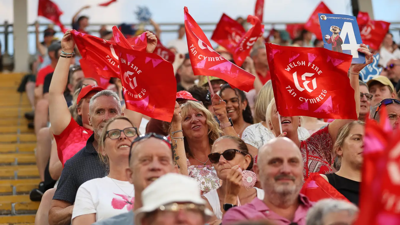 Welsh Fire fans wave red flags in the stands during a cricket match.