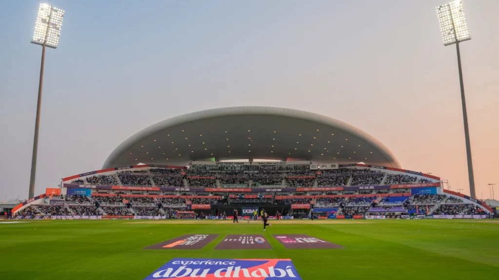 Zayed Cricket Stadium in Abu Dhabi under floodlights during a cricket match.