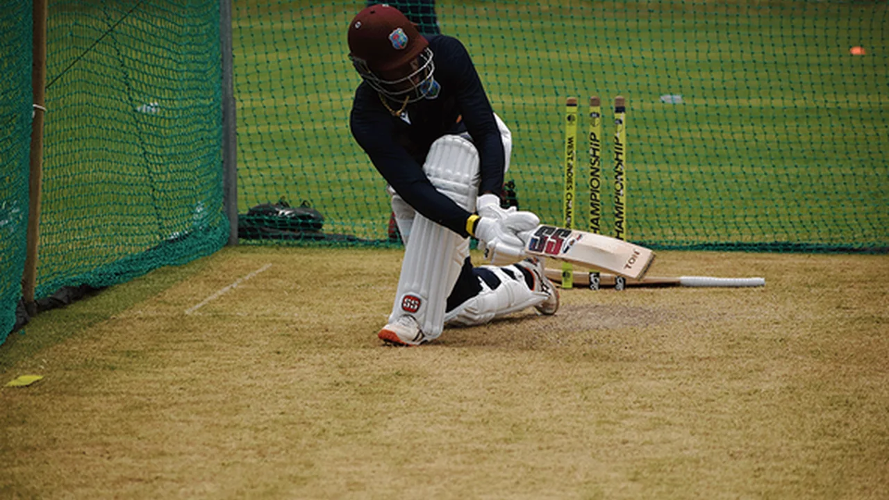 Cricket batter wearing a West Indies helmet plays a sweep shot during a batting practice session in the nets.