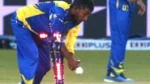 Cricket player in a blue and yellow uniform removes the LED bails from the stumps while holding a cricket ball during a match.
