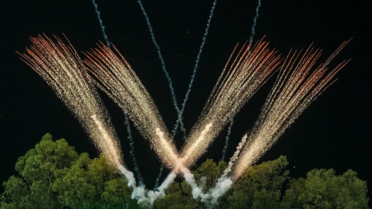 Spectacular golden fireworks illuminate the night sky above trees, creating a dazzling display during a nighttime celebration.