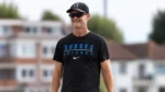 Grant Flower, Surrey County Cricket Club coach, walks across a cricket ground wearing Sussex Cricket training gear and carrying a cricket bat and fielding glove.