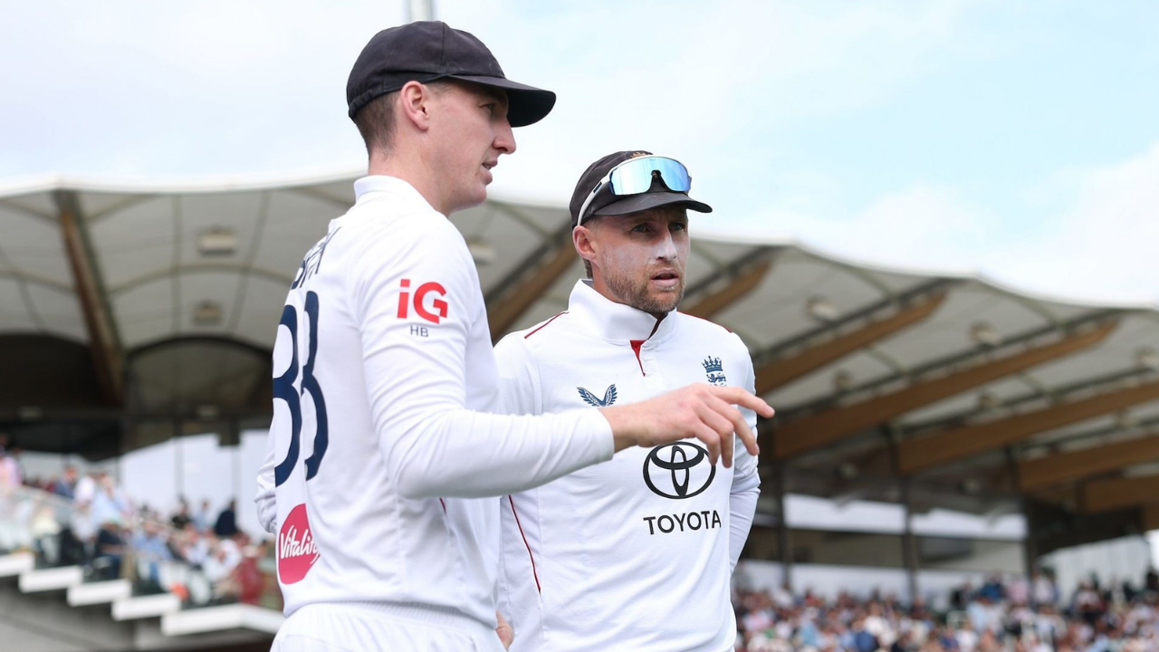 England cricketers Harry Brook and Joe Root discuss tactics on the field during a Test cricket match, wearing white England cricket uniforms.