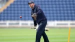 England cricket coach Richard Dawson takes part in a fielding practice session, catching a red cricket ball with a glove on the field.