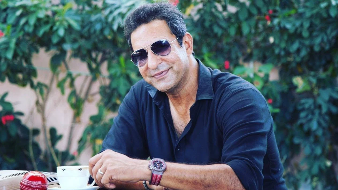 Wasim Akram, former Pakistan cricket captain and legendary fast bowler, wearing sunglasses and a black shirt while sitting outdoors with a cup of tea.